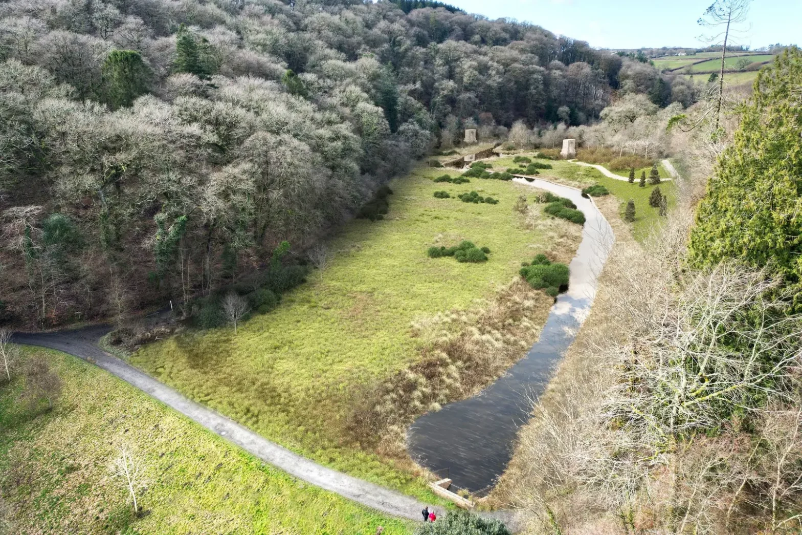 Photorealistic photomontage visualisation showing proposed Arlington Court lake restoration with meandering watercourse, woodland edges and integrated walking paths within natural valley setting.